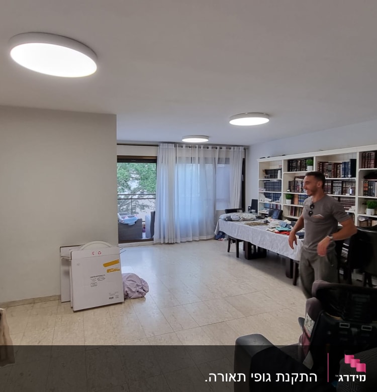 אדם עומד בחדר עם שולחן מלא חפצים